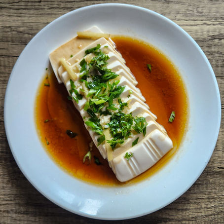 Silken Cantonese steamed tofu sliced and arranged on a plate, topped with soy sauce, ginger, scallions, and sizzling hot oil garnish.