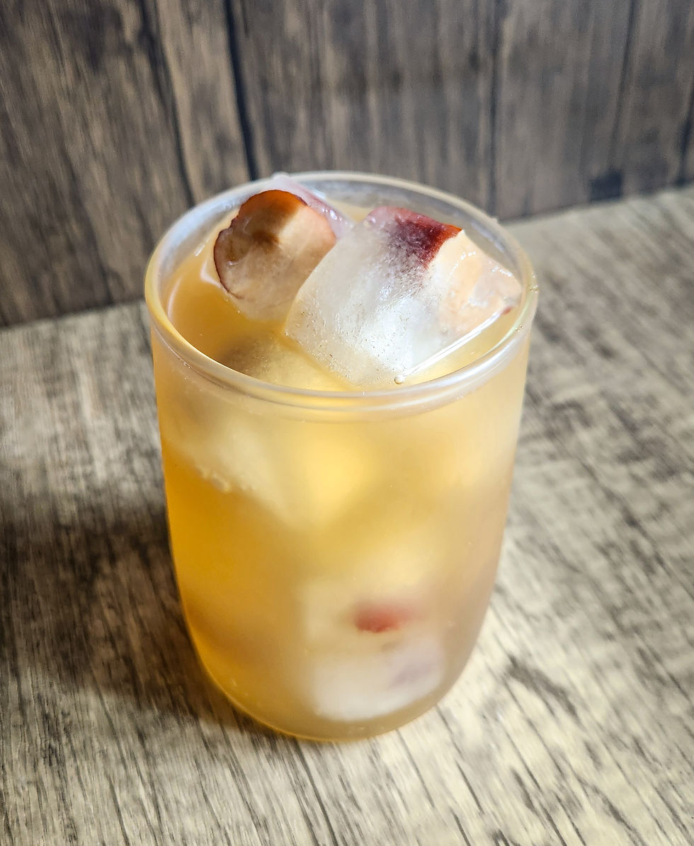 A short glass filled with iced barley tea, featuring visible ice cubes with embedded pieces of red dates.