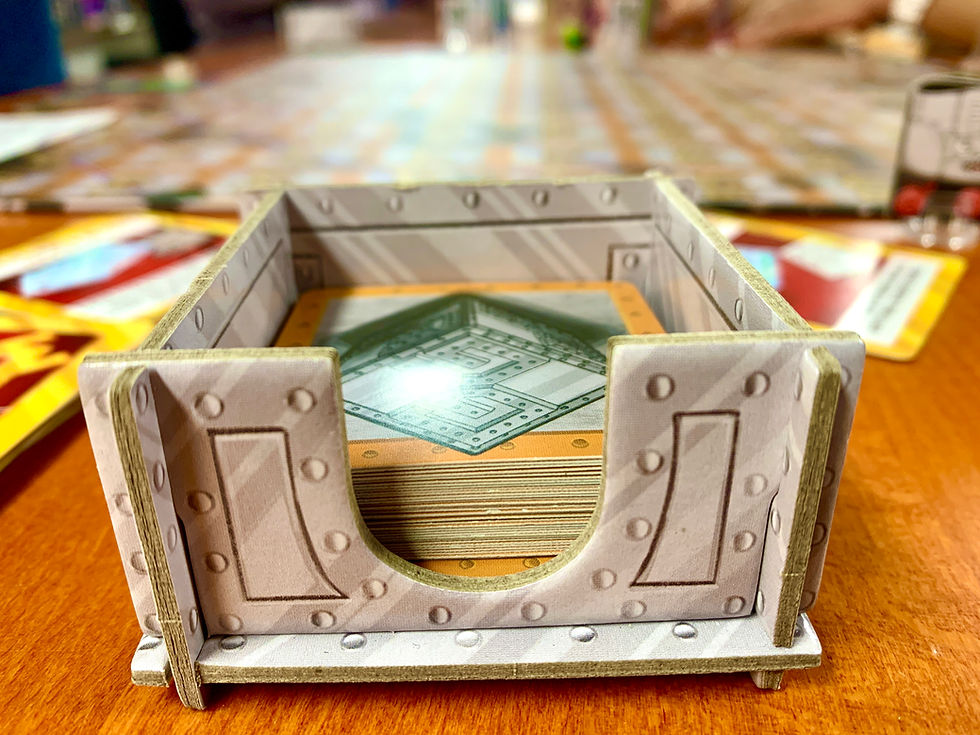 A small cardboard box printed to appear metallic containing a deck of small cards with an orange and steel silver backing.