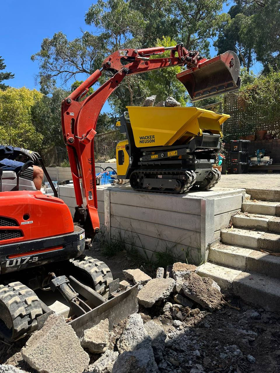 Green Heaven operator using a mini excavator to remove concrete and load it into a dumper during a residential excavation project in Melbourne.