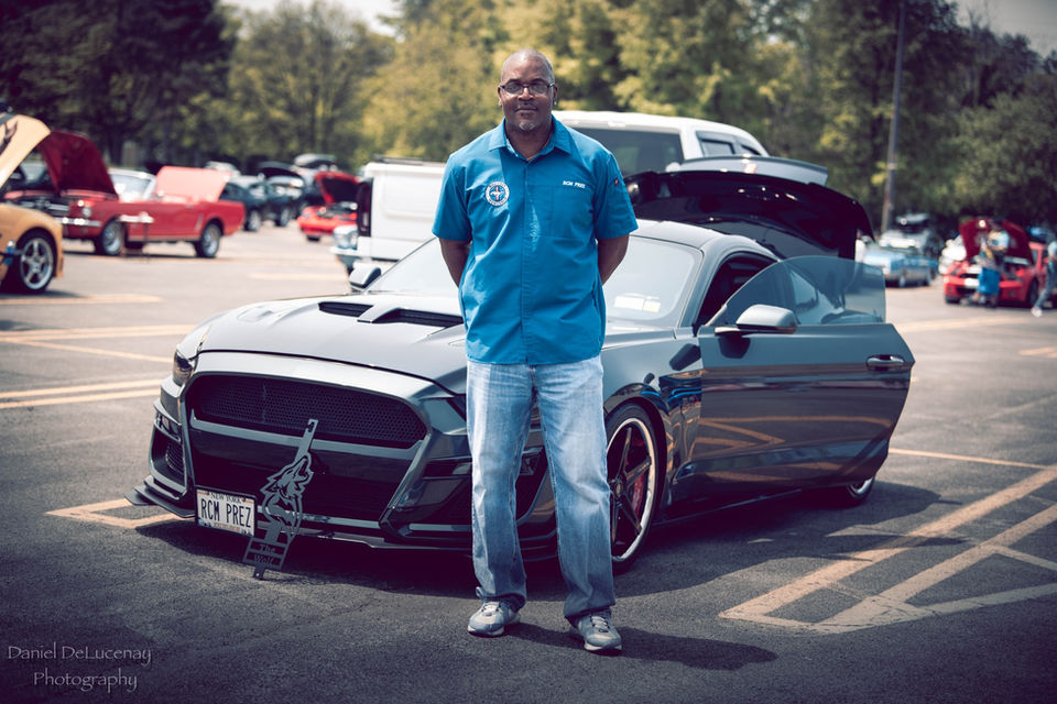Man proudly stands beside his modified Mustang