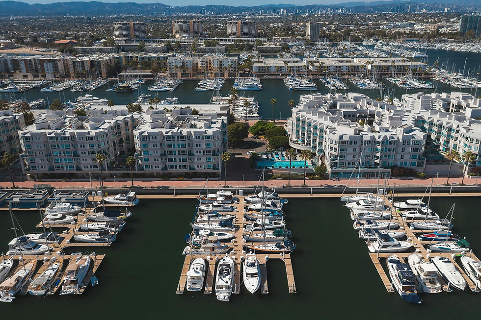 Aerial view of Marina del Rey showcasing its bustling marina filled with boats and yachts, surrounded by modern waterfront residences under a clear blue sky.