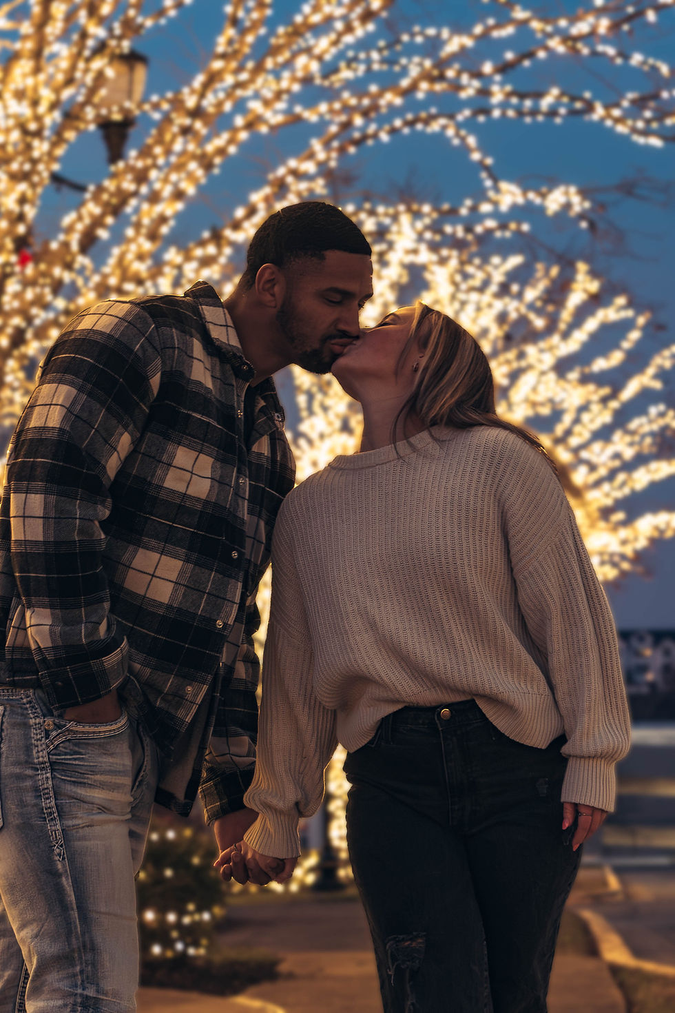 Romantic nighttime portrait of a couple kissing and dancing in front of glowing warm yellow string lights