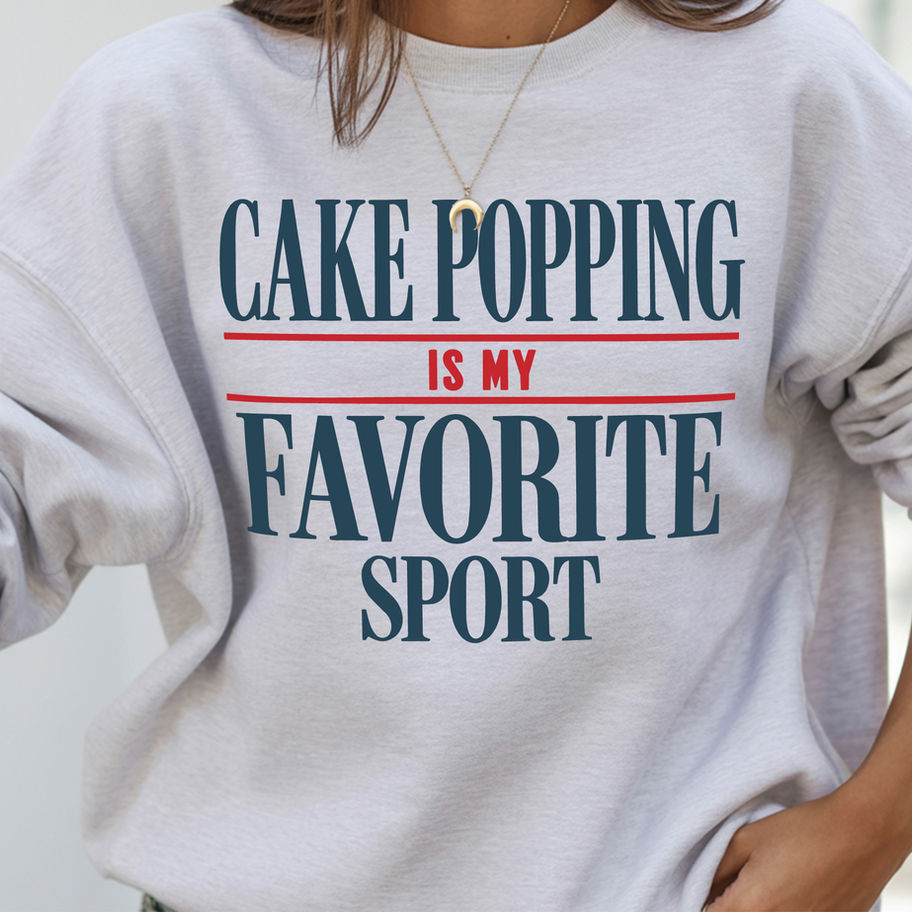 Woman wearing a light grey crewneck sweatshirt featuring the text Cake Popping is my Favorite Sport