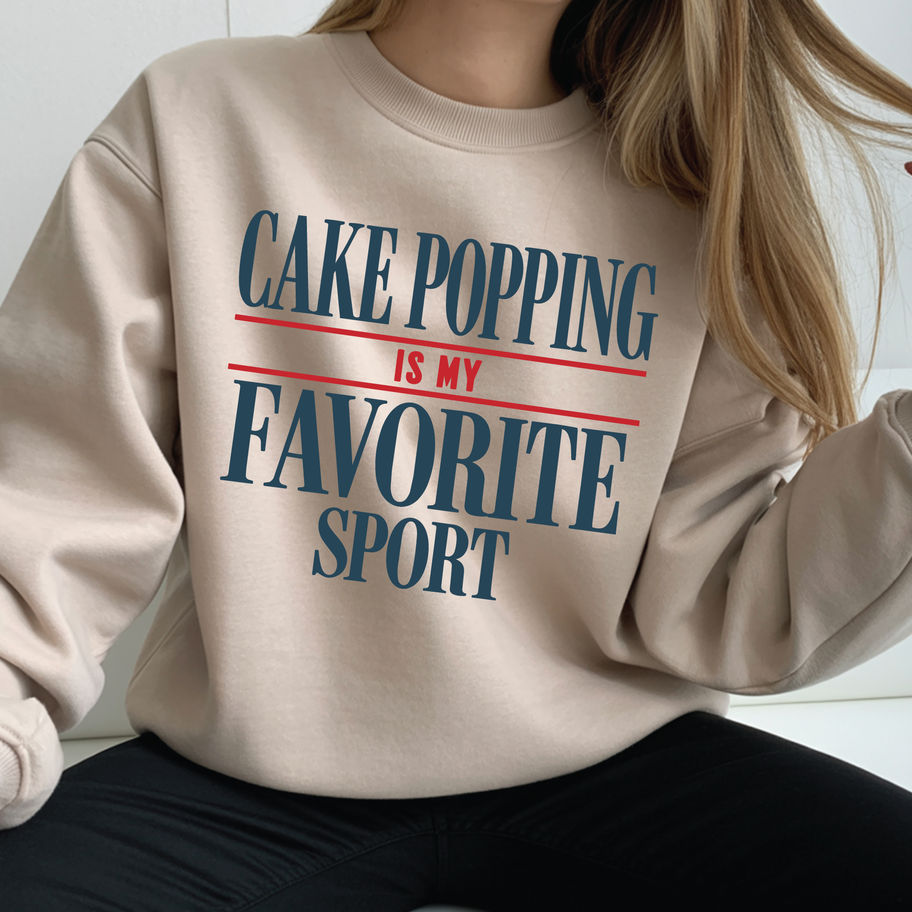 Woman modeling a beige crewneck sweatshirt with the Cake Popping is my Favorite Sport graphic