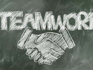 the word teamwork written on a blackboard with hands shaking