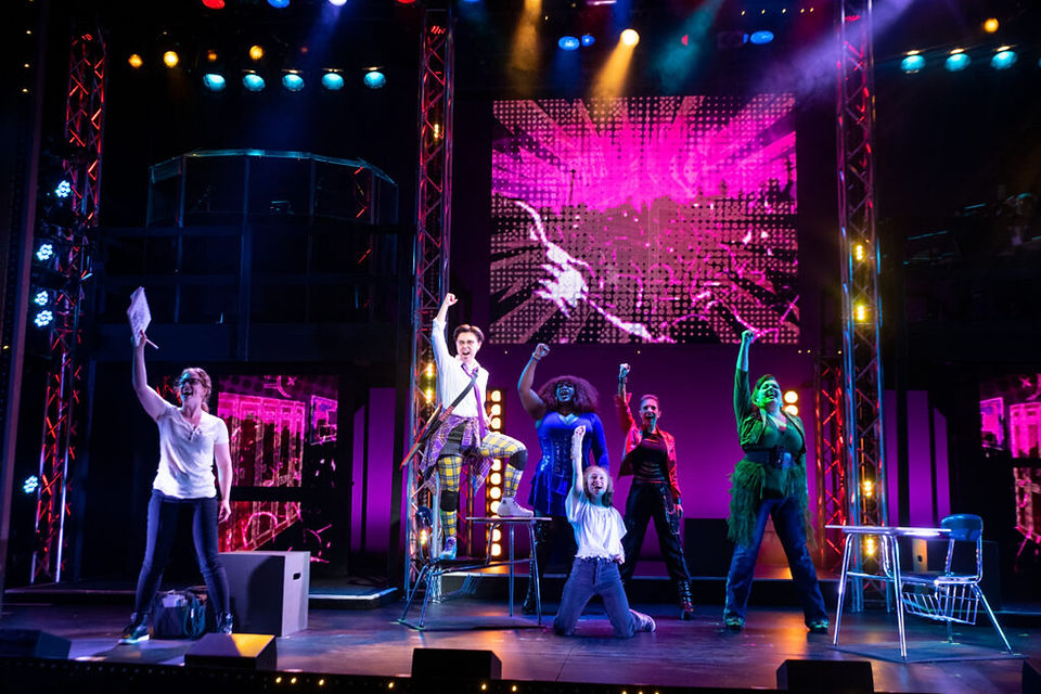 SuperYou musical cast and superheroes performing together beneath colorful stage lighting and video screens, enhanced by zactrack SMART real-time tracking for automated backlighting and creative lighting effects.