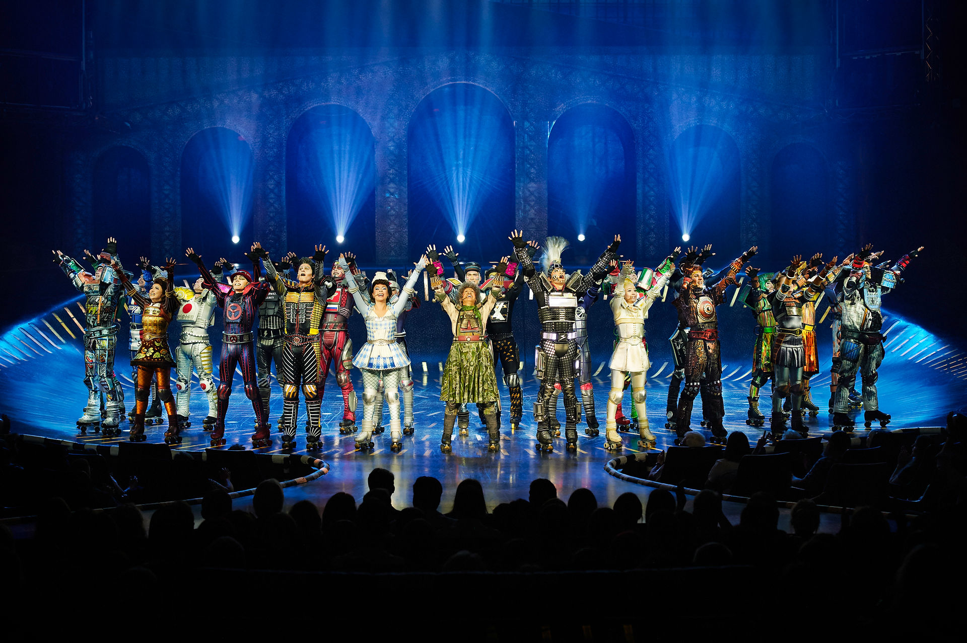 Starlight Express full cast celebrating together on the arena stage in colorful roller-skating costumes, illuminated by 30 moving lights connected to the zactrack PRO real-time tracking system.