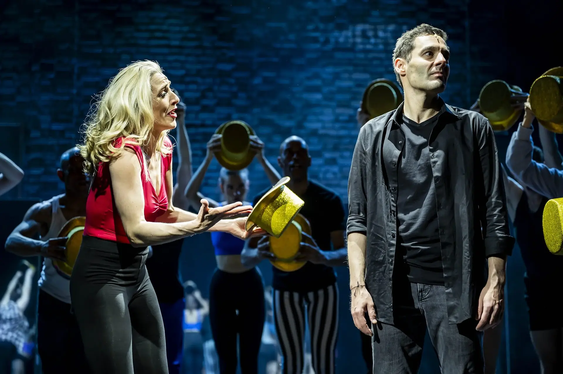 Two lead performers in A Chorus Line at First Stage Theater Hamburg, surrounded by ensemble members holding gold hats, with theatrical blue lighting and zactrack SMART automated tracking supporting accurate followspot positioning as performers move across the stage.