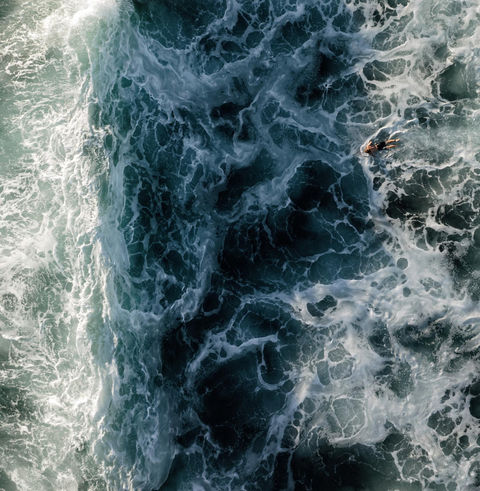 Drone shot of surfer about to dive unter a wave.