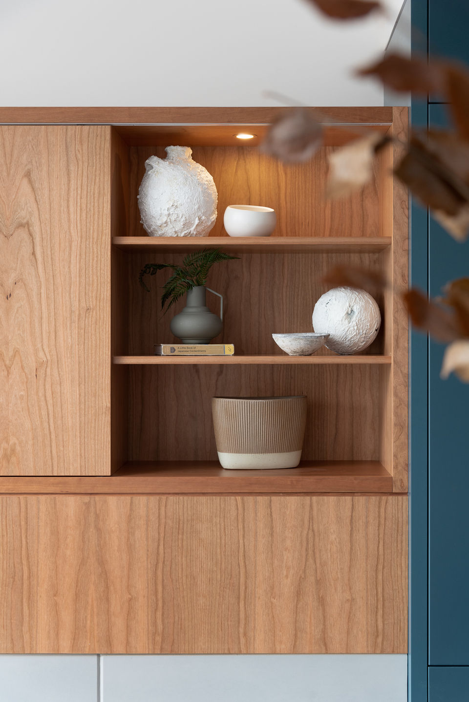 Vignette of cherry wood custom designed media unit. Open shelving with puck lighting.