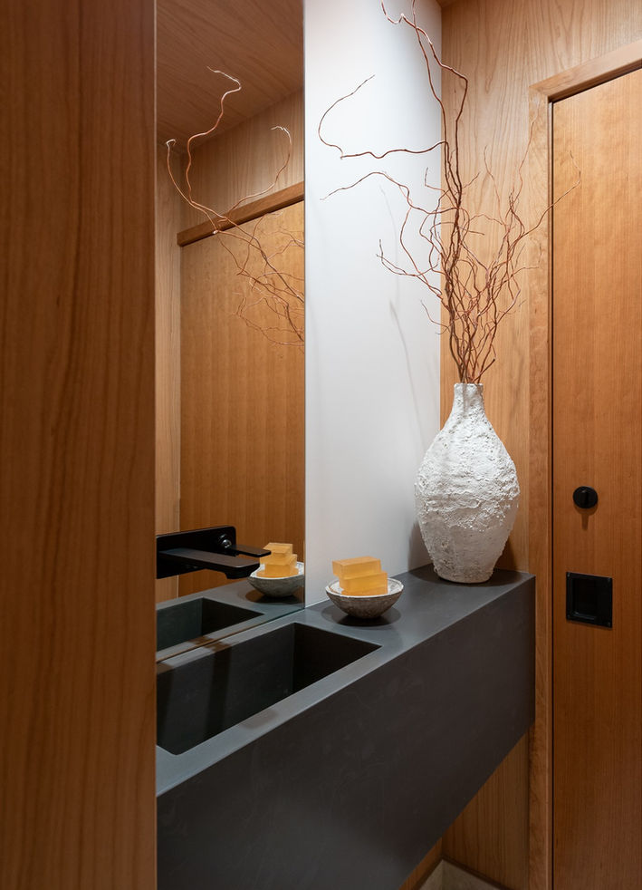 Powder room with a small footprint. Wood veneer walls and ceiling. Wall mounted black faucet. Custom sink and counter made of corian.