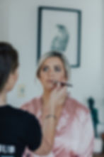 Makeup artist applying lipstick during bridal prep, pink satin robe