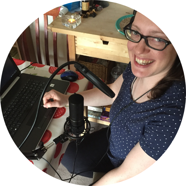 Woman sitting at table with laptop and microphone in front of her. She is smiling towards the camera