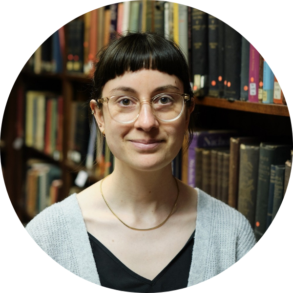 Woman facing towards the camera, smiling, with shelves of books in the background.