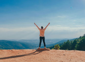 Frau seht oben auf einer Platte ganz weit oben in den Bergen, blickt in die Ferne und genießt die Aussicht mit nach oben gerichteten Armen