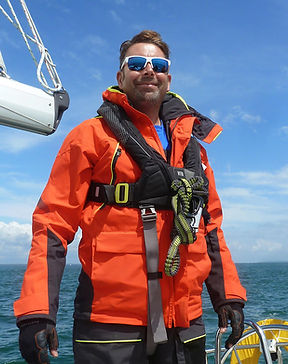 Anthony Bream smiling on sailboat, orange jacket, life vest