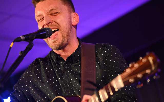 Close-up of Tom Ryder singing under a purple stage light at an evening wedding party