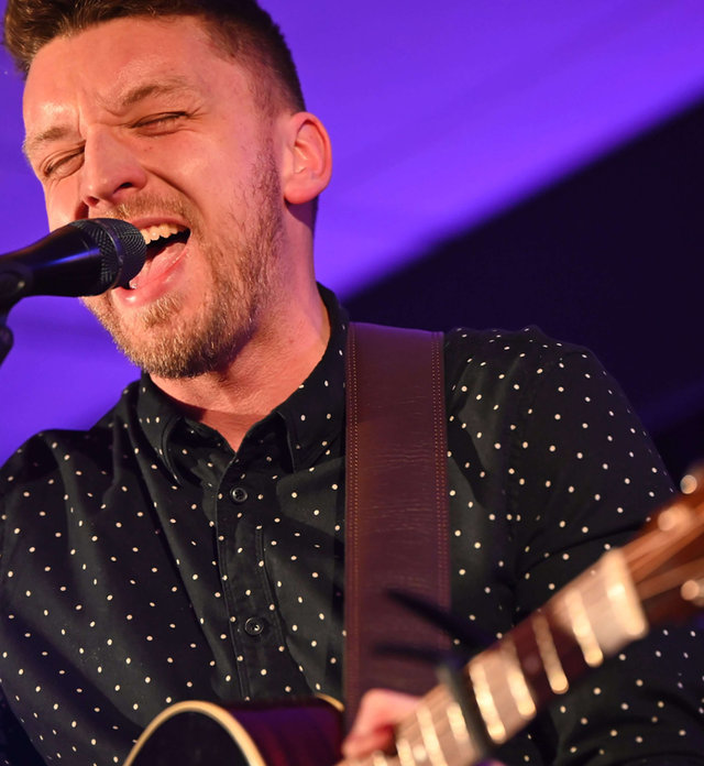 Close-up of Tom Ryder singing under purple stage light