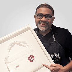 Ajay John smiling and pointing to a framed MasterChef bag