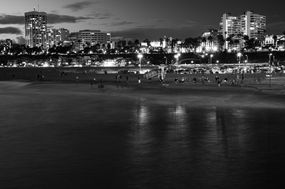 Black and white Santa Monica beach at night with city lights.