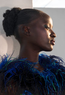 Elegant woman with dark skin in profile, blue feathered top, indoors, natural light.