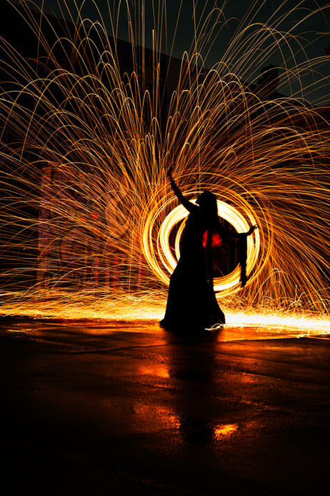 Silhouette figure holding fiery steel wool, creating a glowing circle, dark background.