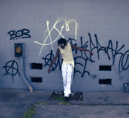 a purple toned photo of a man walking in front of a wall of graffiti 
