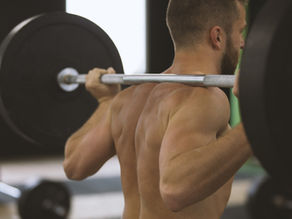 Man lifting a heavy barbell in a gym. Focused expression, muscular back visible. Blurred background with gym equipment.