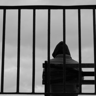Person in hoodie sweatshirt sitting behind fence