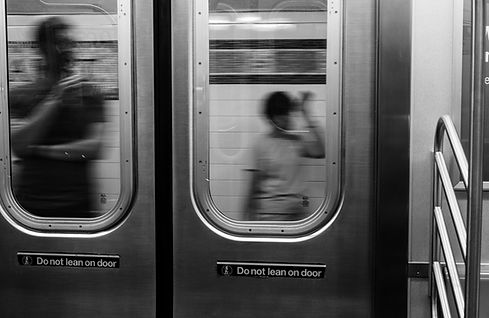 Blurred image from inside a subway car looking out onto the platform with people waiting