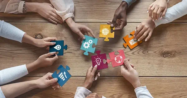 Several team members placing their piece of the puzzle in the center of the table