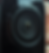 Close-up of a black camera lens with concentric circles, reflecting light. Background is blurred with warm tones.