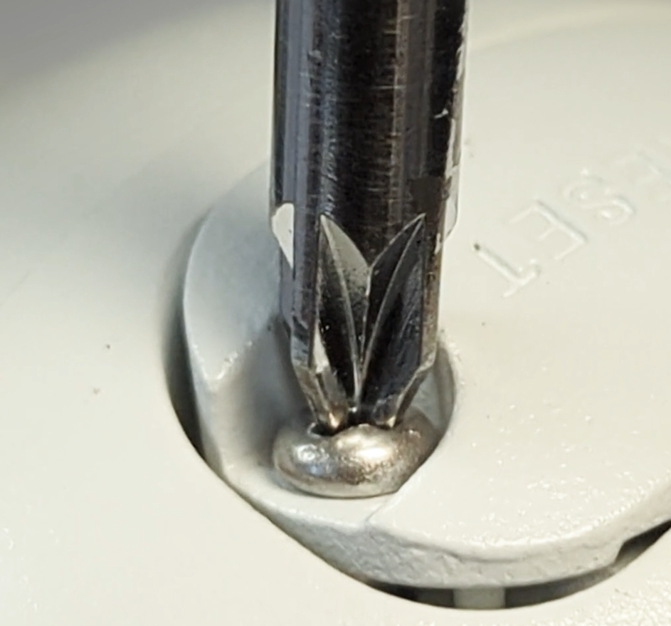 Close-up of a metallic Phillips screwdriver engaging a screw in a light gray surface, with embossed text "SET" partially visible.
