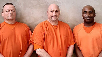 Three men in orange prison uniforms pose proudly