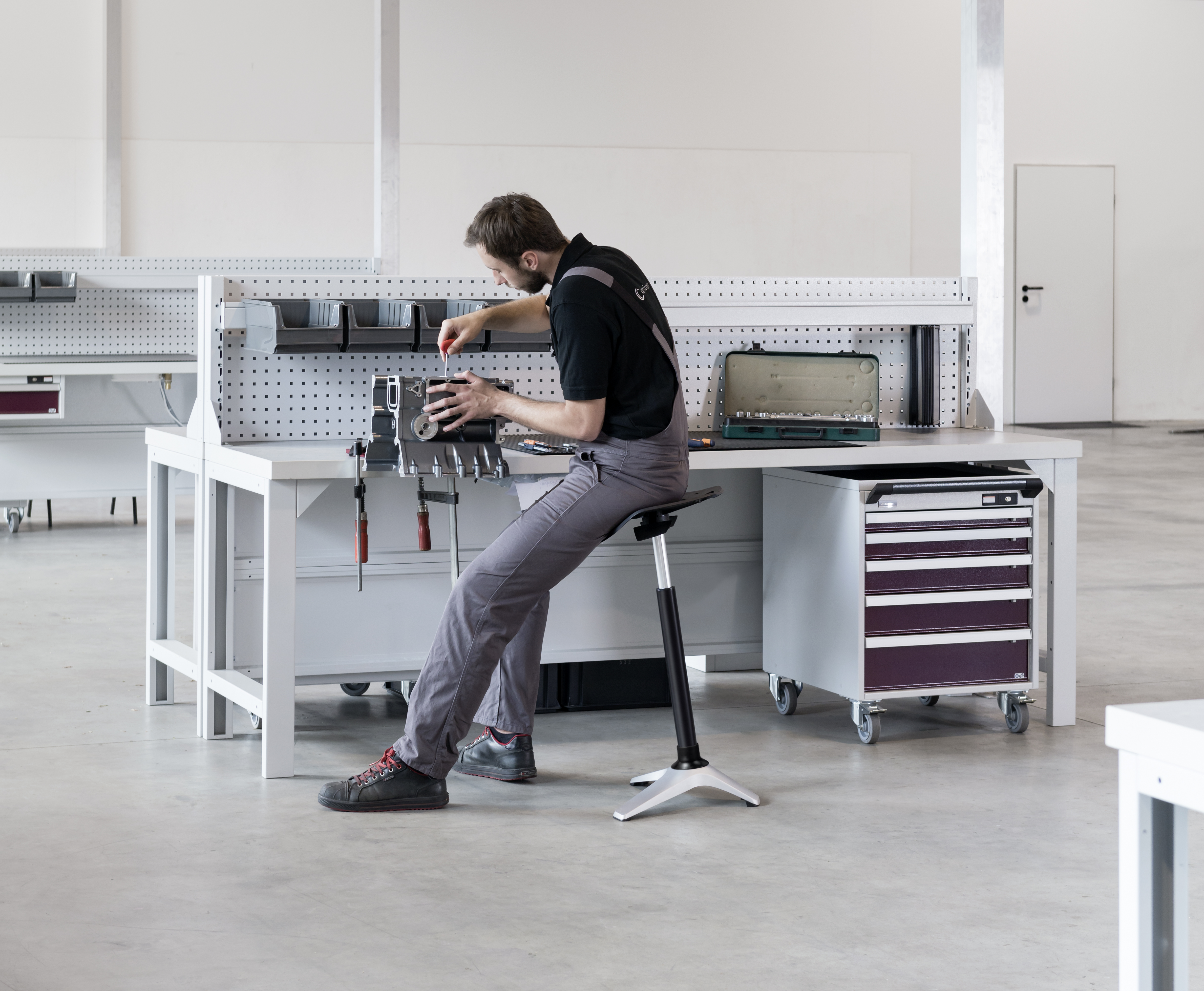 Mann arbeitet ergonomisch an Werkbank mit ONGO Stand Stehhilfe in Industrieumgebung