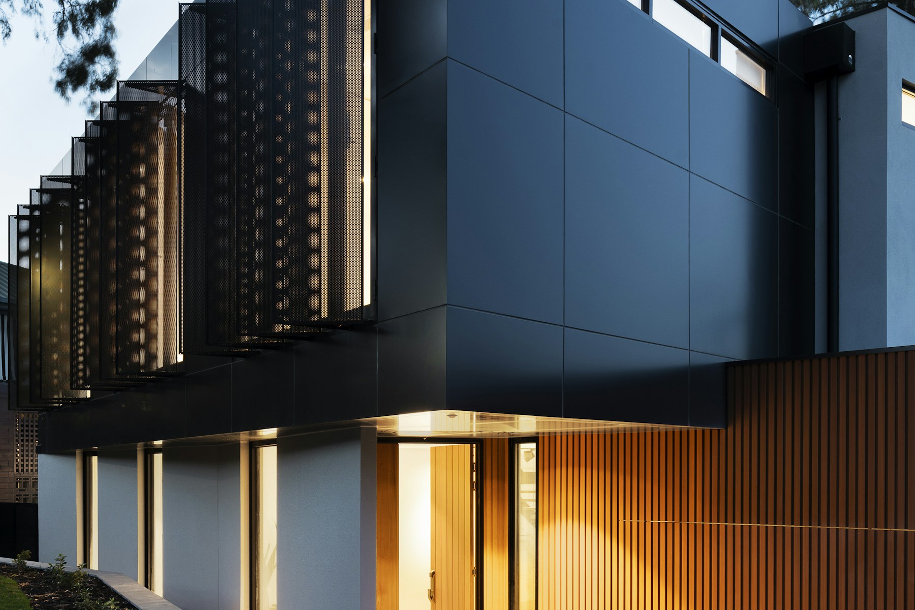 Night entry of a modern rental with wood slats and a lit front door