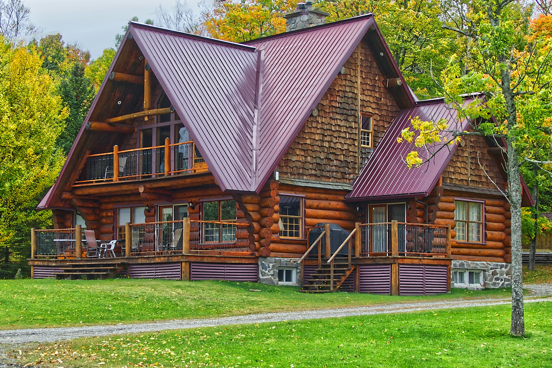 Log-cabin rental with a burgundy metal roof and a wraparound deck