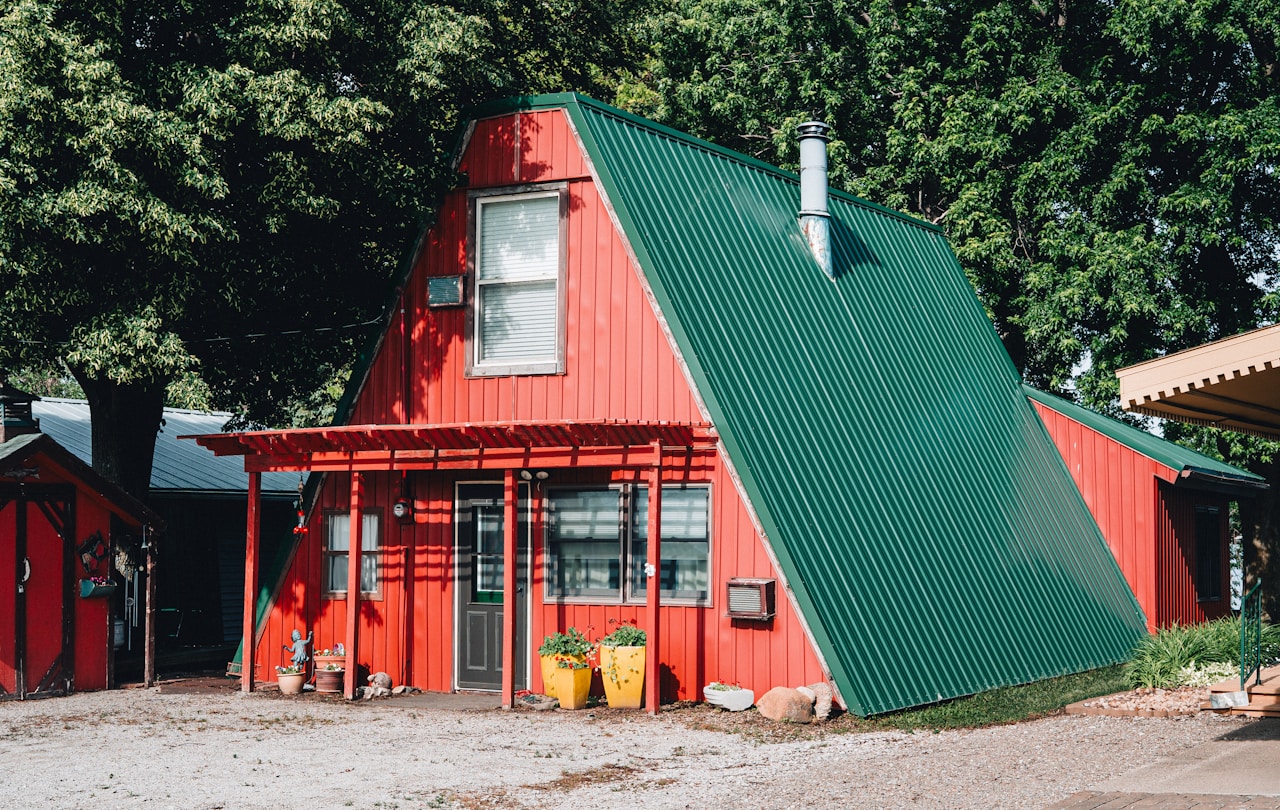 Red A-frame cabin with a green metal roof among trees