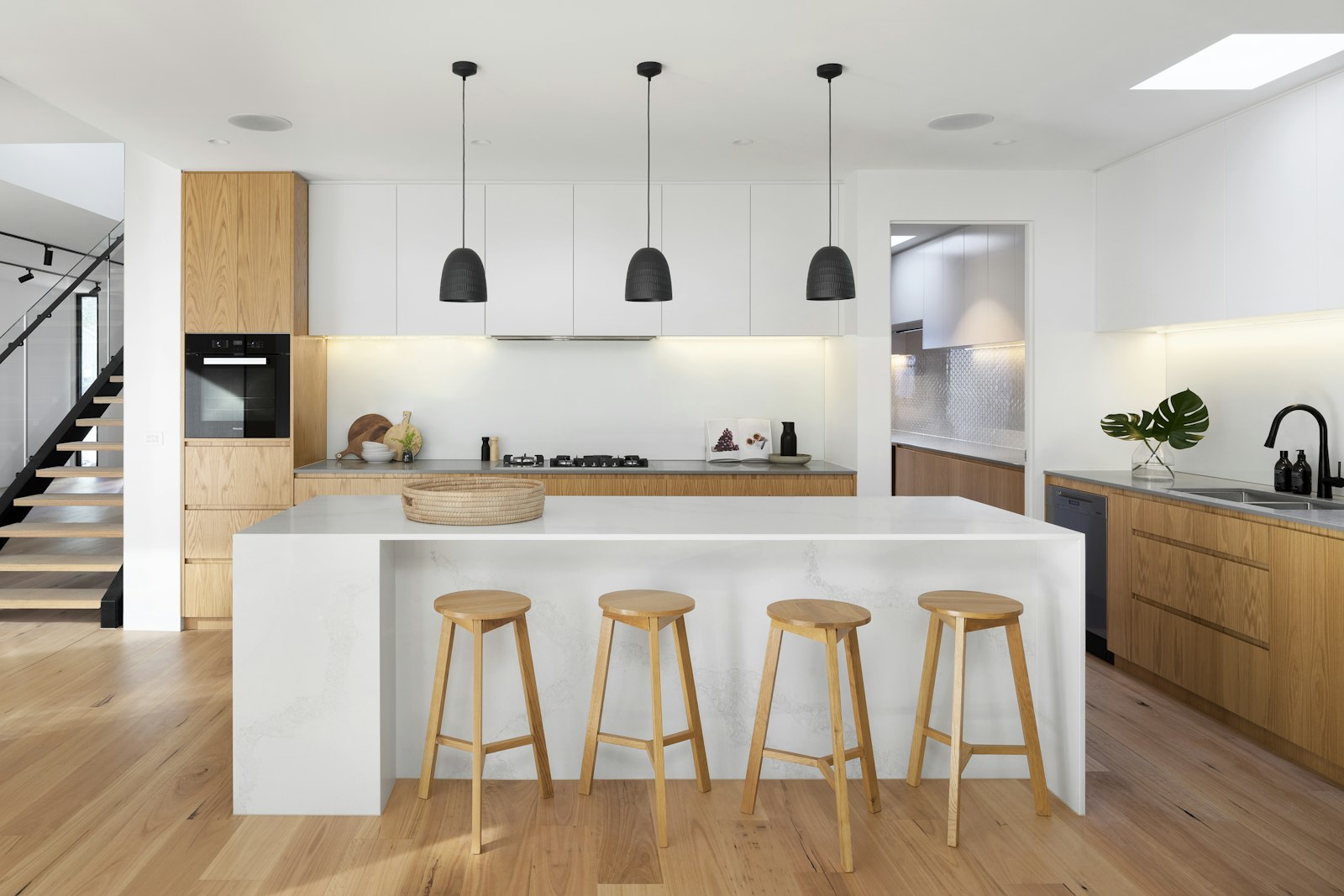 White oak kitchen with a marble island and four stools, no people