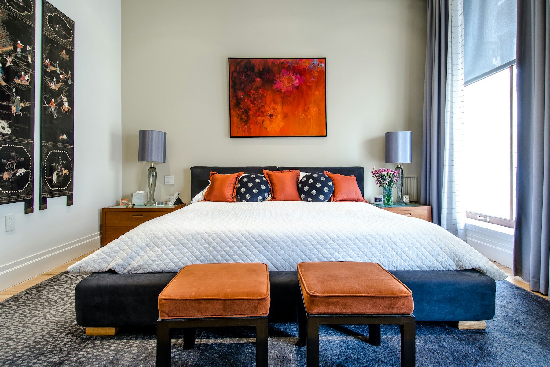 Rental bedroom with orange ottomans and a floral painting