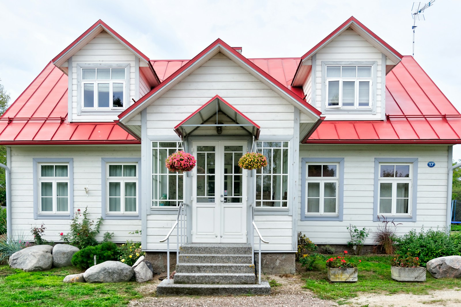 White cottage with red metal roof and hanging baskets, no people