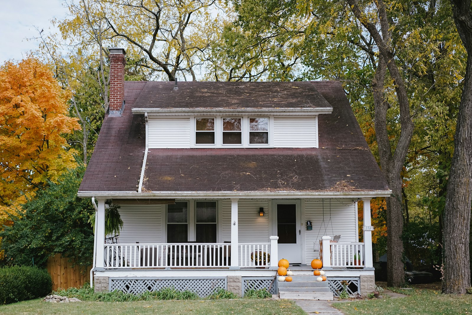 White porch house in autumn trees with pumpkins on the steps