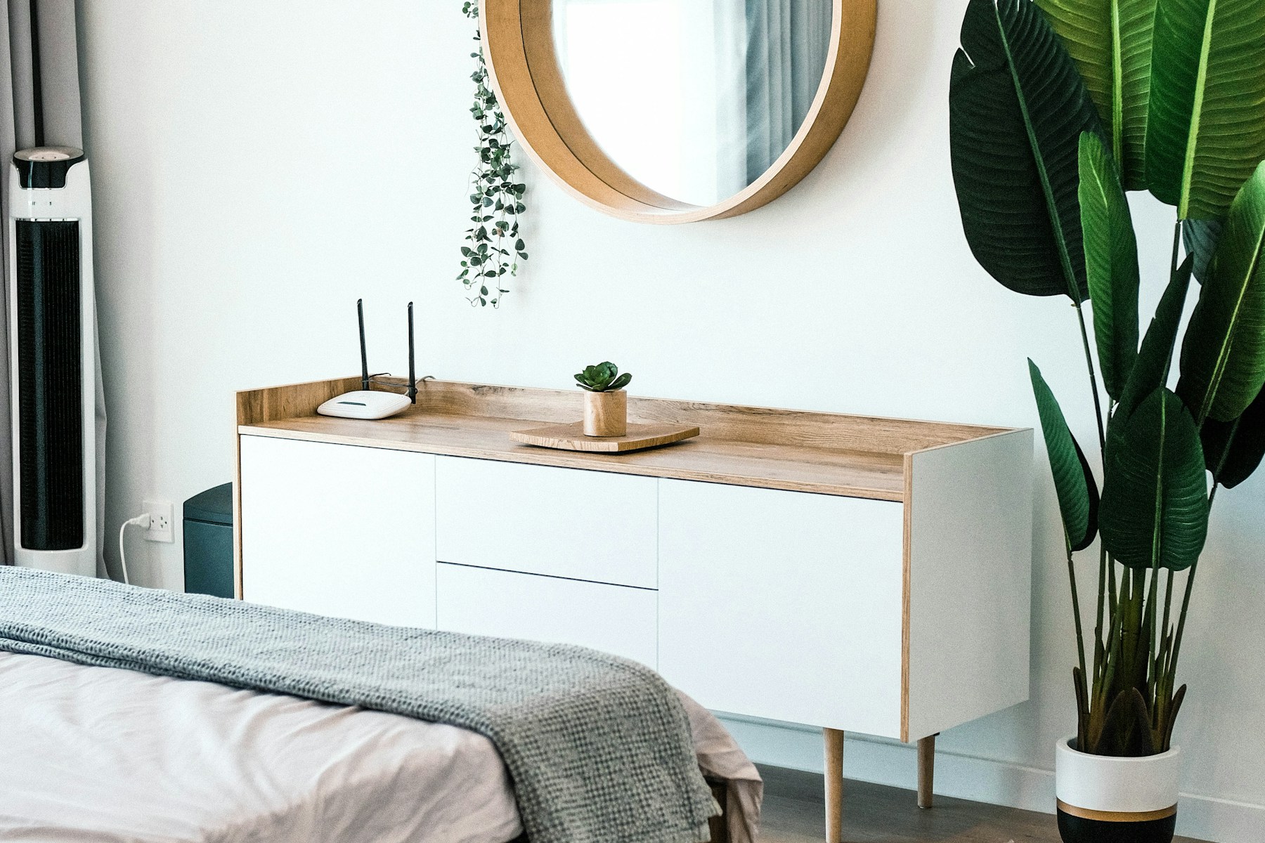 Bedroom dresser with a round wood mirror and a tall plant