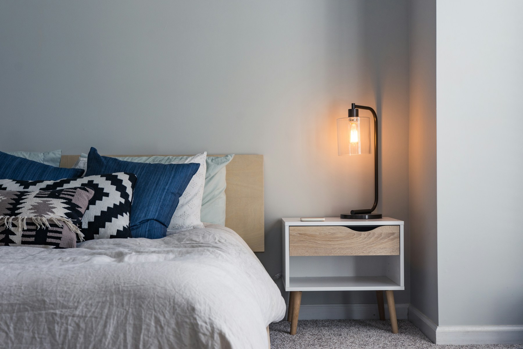 Rental bedroom with blue pillows and a glass nightstand lamp