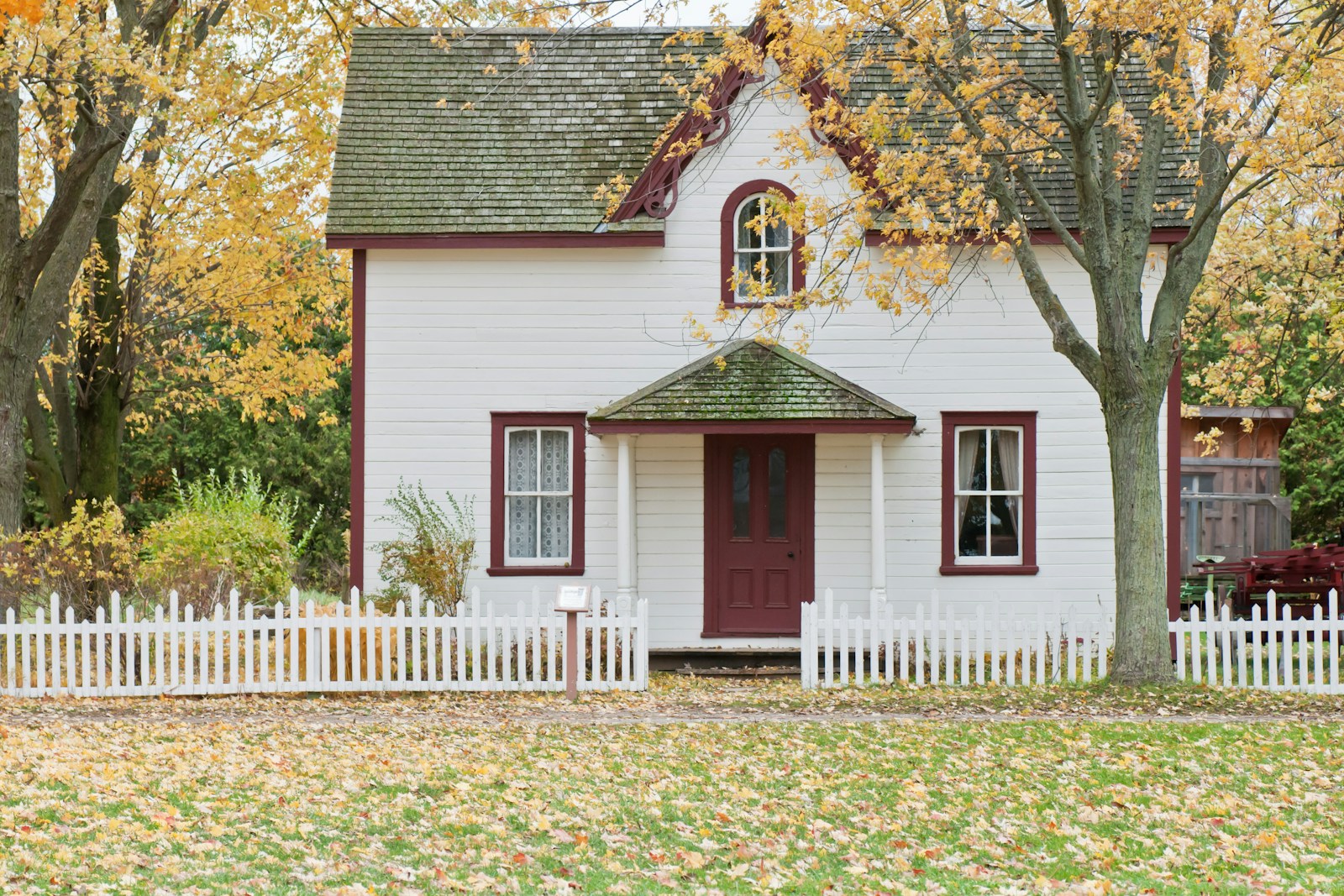 White farmhouse with picket fence and autumn trees, no people