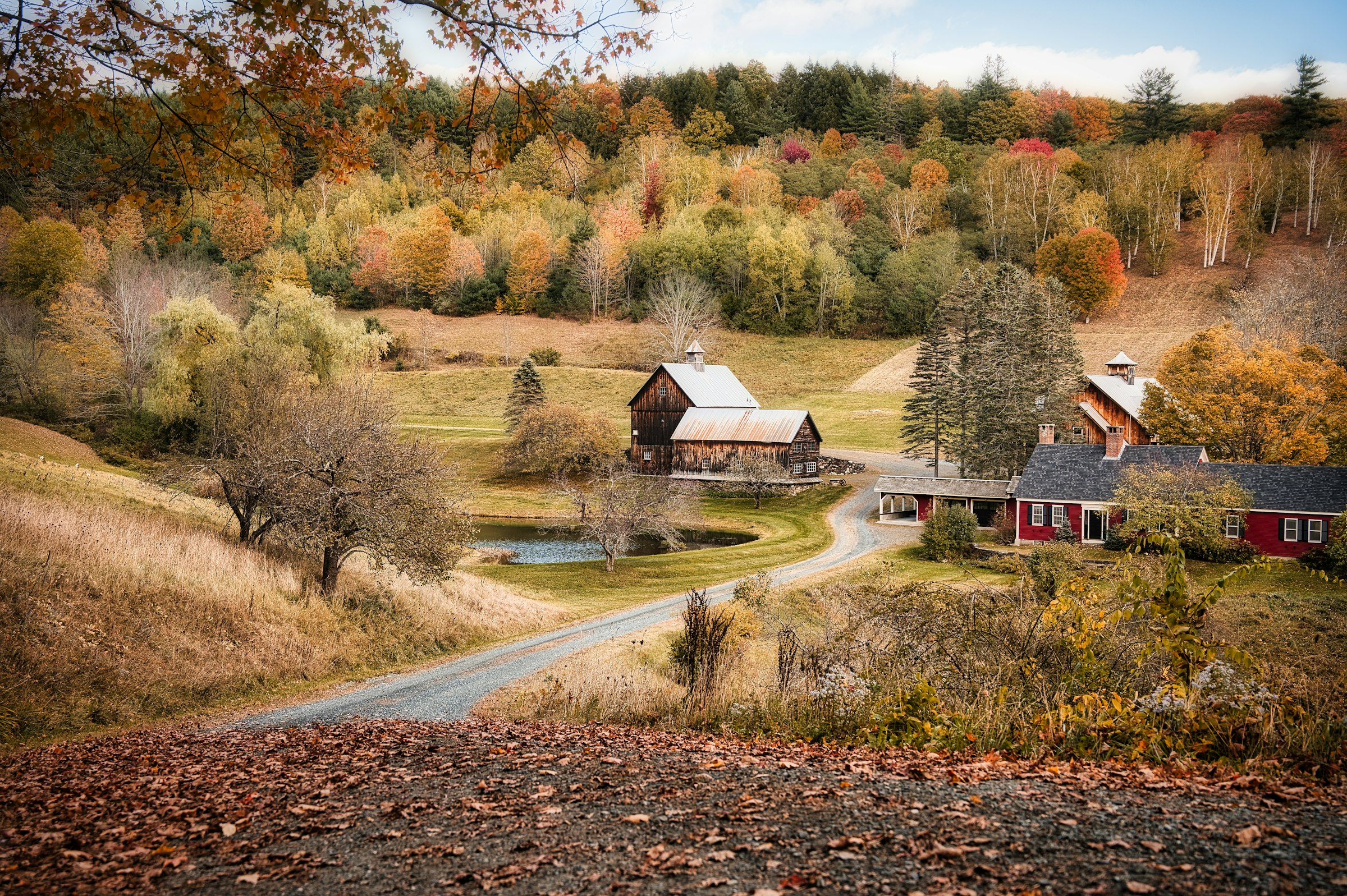 Farm buildings, autumn trees, and a river valley in Woodstock, Vermont. Unsplash photo location-tagged Woodstock.
