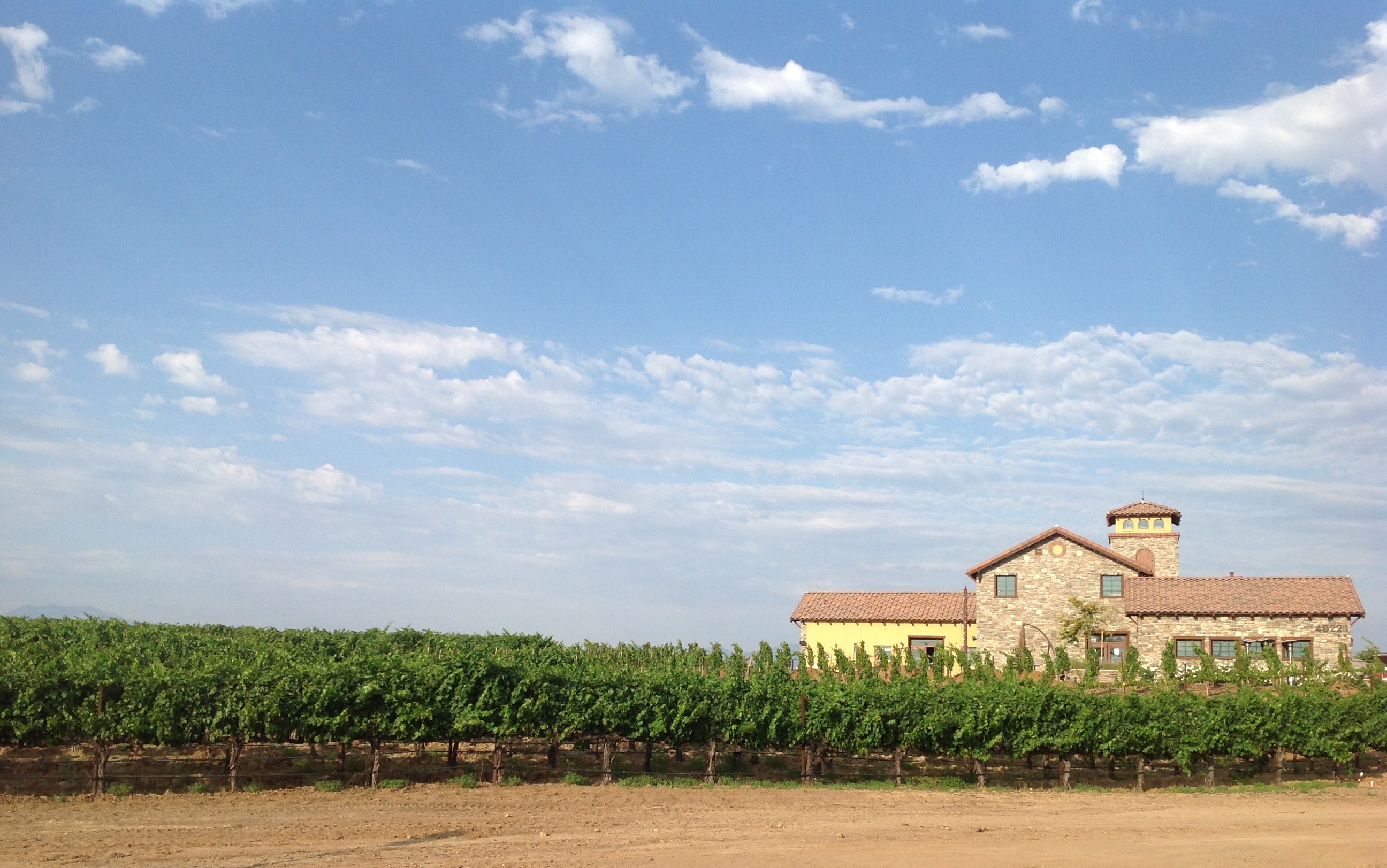Stone Temecula winery beside green vineyard rows