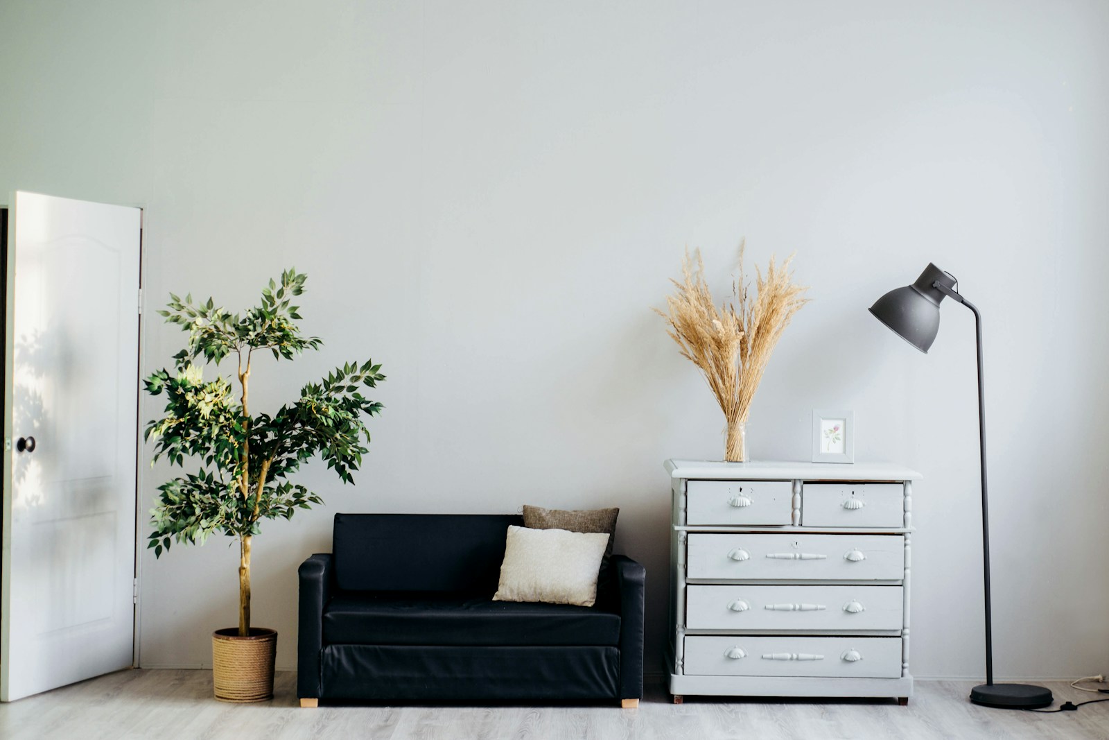 Small black sofa, dresser, and plant against a pale wall, no people