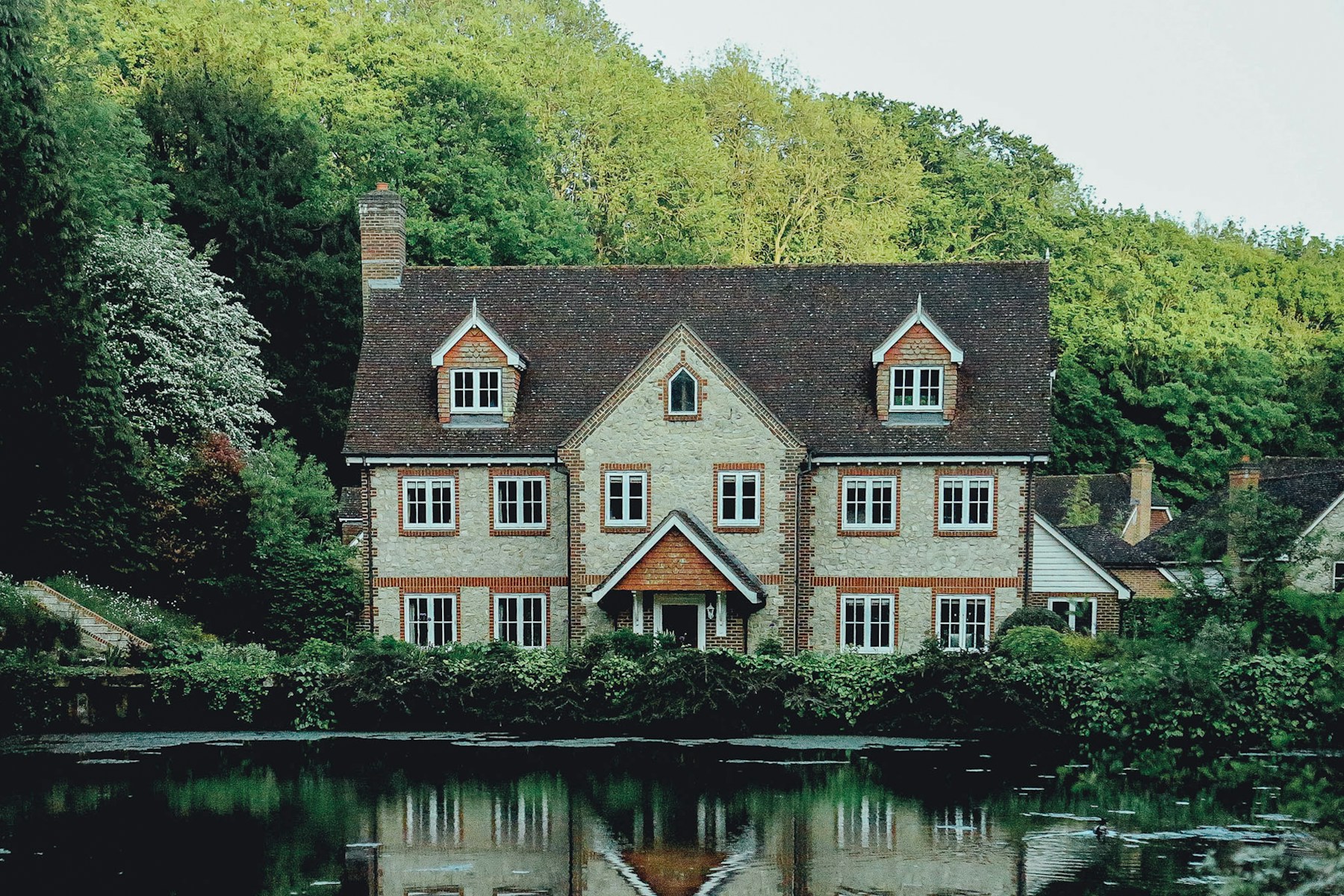 Stone rental house reflected in a pond with woods behind it